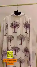 Watch as إبرة و خيط🧵🪡 showcases a stunning white maxi dress adorned with a bold purple palm tree print. This stylish piece is displayed on a modern gold clothing rack, paired perfectly with elegant black heels. The simple yet chic presentation highlights the dress's design, making it ideal for casual outings or beach vacations. by @needle_t with original sound
