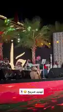 This is a live performance by a traditional musical ensemble during a nighttime cultural event. Musicians dressed in regional attire play a variety of instruments, including stringed instruments and percussion, on an outdoor stage. The stage features palm trees, decorative lighting, and a large illuminated sign, creating an atmospheric setting for the concert. by @jalsahevent with jalsahevent by Original Sound