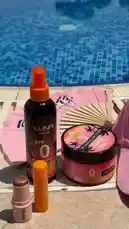 A serene poolside scene showcases a curated collection of Luna Sun Tan sun care products, including a spray bottle, tanning balm, and lip balms. The setting evokes a relaxing summer day by the water, perfect for enjoying beauty essentials in a tranquil environment. by @bx301a with BARA🇧🇷🔥🌬️ by Contains: Ritmadinha Trajado de Lacoste - MC VN Cria