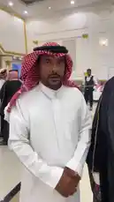 This video features Khaleefa Eid, dressed in traditional Middle Eastern attire, including a white thobe, red-and-white checkered ghutra, and a black bisht with gold embroidery. He is seen smiling and speaking in what appears to be a formal gathering or event hall. The setting includes other attendees in similar traditional clothing, suggesting a cultural, religious, or official occasion. by @kh-p19 with kh-p19 by Original Sound