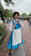 A woman dressed as Belle from Disney's 'Beauty and the Beast' greets a visitor named Manira at a theme park. She smiles warmly and waves her hand in a friendly gesture, creating a magical meet-and-greet moment. by @moneeragh with Original Sound by moneeragh