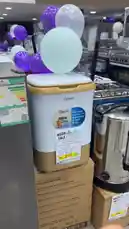 This video features a detailed look at the Clikon 3-in-1 mini washing machine, showcasing its compact design and functionality. A hand opens the lid to reveal the interior drum, while a price tag clearly displays '220 SAR' during a 'MEGA SALE'. The product is presented on a cardboard box in what appears to be a retail store setting, with Arabic text on the packaging and promotional balloons in the background. by @dalilnet with Original Sound by dalilnet