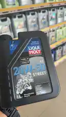 A close-up, handheld shot of a Liqui Moly 20W-50 Street motorcycle oil bottle being displayed in a retail store aisle. The black plastic container features prominent branding, including 'Made in Germany,' 'Motorcycle,' and 'Mineralisches Motoröl.' The label clearly shows the viscosity grade '20W-50' and 'STREET,' along with a graphic of a motorcyclist. The background reveals shelves stocked with various automotive products, suggesting a hardware or auto parts store setting. by @hawkar_service with original sound