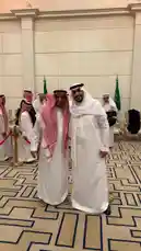 In a formal diplomatic setting, Saudi Prince Bader Alodah is seen shaking hands and posing for photographs with a senior official wearing traditional white thobe and red-and-white patterned ghutra. The event takes place indoors in a grand hall adorned with Saudi Arabian flags and elegant architectural details. Other dignitaries in traditional attire stand in the background, suggesting a high-level state meeting or reception. by @guruofmarketing with original sound