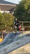 This dynamic clip captures Vepace performing impressive freestyle tricks on his electric dirt bike at a skatepark. He executes a series of jumps and grinds on ramps and rails, showcasing his skills against a backdrop of trees and a large stadium structure. The action is set to energetic rock music. by @vepace with Original Sound by vepace
