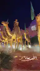 This captivating night scene features a majestic golden camel caravan installation, likely part of a cultural or promotional event in Riyadh. Riders in traditional attire guide the illuminated camels across a desert-themed stage, with mist adding atmosphere. A prominent 'Boulevard' sign and Saudi flag suggest a location like Boulevard Riyadh City. The Arabic text 'الاربعاء' (Wednesday) and time stamp '7:53 PM' confirm the specific evening setting, creating a powerful visual narrative. by @guruofmarketing with original sound