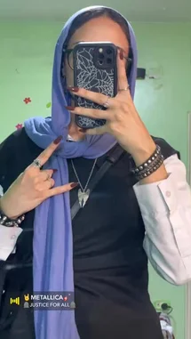 Watch Hana 𓋹 showcase her unique personal style in this mirror selfie. She pairs a vibrant purple hijab with bold dark nail polish and multiple rings, making a 'rock on' hand gesture. Her phone case features a spiderweb design, complementing her layered black top and white shirt sleeves. A 'METALLICA JUSTICE FOR ALL' sticker in the corner reveals her love for the legendary band, blending cultural modesty with a fierce rock aesthetic. by @inxhell with 🤘METALLICA🎸 by 🪦JUSTICE FOR ALL🪦