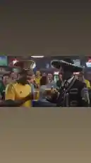 In a lively sports bar, two football fans—one supporting South Africa and the other Mexico—engage in a humorous conversation about their national team loyalties. The man in the traditional Mexican charro suit explains his support, while the South African fan jokes about job competition. The scene captures a fun, light-hearted moment of international camaraderie among fans during a big game. by @be-sassyish with Original Sound by be-sassyish