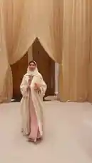 A woman in a stunning white hijab and matching outfit confidently walks down a runway-like path. She holds a clutch and carries herself with grace against a backdrop of elegant beige curtains. This stylish presentation showcases modern modest fashion, reminiscent of celebrity style trends. by @soja_design with original sound