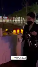 A woman in a black outfit and face mask prepares coffee using a silver carafe at an outdoor event table adorned with candles and red flowers under the night sky. by @jalsahevent with jalsahevent by Original Sound