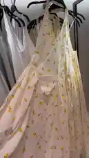 A stylish, cream-colored maxi dress with a delicate yellow floral pattern is showcased hanging on a black hanger in a modern clothing store. The camera pans slightly to reveal another yellow ruched dress beside it, highlighting contemporary women's fashion. The bright, minimalist setting emphasizes the garment's design, suitable for spring or summer wear. by @ru.ab71 with Original Sound by ru.ab71