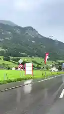 Experience a breathtaking journey along a wet road winding through lush green valleys and charming alpine villages nestled against the majestic Swiss Alps. This immersive drive showcases traditional architecture, vibrant flag banners fluttering in the breeze, and the serene beauty of rural Switzerland under a soft, overcast sky. by @sahab-alalam with sahab-alalam by Original Sound