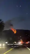 tufavlatiino 님이 만든 Original Sound 포함 @tufavlatiino 님이 만든 A stunning and alarming view of a large fire burning on Mount Hamilton in San Jose, CA, captured from a moving vehicle at night. Bright orange flames and thick smoke rise into the dark sky, illuminating the surrounding hills and the city lights below. The footage provides a real-time perspective of the wildfire event.