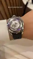 A close-up view of a sophisticated mechanical watch worn on a wrist. The timepiece features a transparent case back, revealing intricate internal gears and a purple accent ring. It has a silver-toned case, a black strap with purple stitching, and a crown on the side. The background shows a white shirt cuff and a wooden surface. by @lussowatches with Helicopter by India version 😂