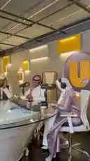 A behind-the-scenes look at a live podcast recording session at UFM Radio. The modern studio features several hosts, including men and women dressed in traditional Middle Eastern attire like thobes and hijabs, seated around a large glass table with professional microphones and headphones. The atmosphere is focused and professional, capturing the essence of contemporary Arabic radio broadcasting. by @ufmradio with شغل معلمين 👌 by Sn: hamadi_568