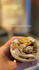 A hand holds a freshly prepared shawerma wrap from Alremal Shawerma, showcasing tender layers of seasoned meat, crisp vegetables, and creamy sauce nestled within soft flatbread. The focus highlights texture and flavor, inviting viewers to experience the culinary artistry behind this popular dish. by @sandshawarma with original sound