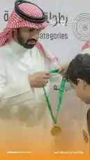 A dignitary in traditional Saudi attire presents a gold medal on a green ribbon to a young recipient during an awards ceremony hosted by the Player Association. The event celebrates achievements in sports, with branding for the 'Player Association' and 'Al-Nassr Club' visible in the background. by @playerassoc with original sound