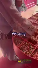 This close-up video offers a stylish glimpse into a boutique setting, focusing on a person's hand reaching into a vibrant pink organizer filled with colorful buttons and beads. The individual is wearing a light-colored sweatshirt with floral and star embroidery. The word 'Blushing' is displayed on screen, suggesting it's part of a brand or collection name. by @bx301a with 🌴🌴🌴🌴🌴 by Contains: HOT UPTOWN - Camila Cabello, Drake