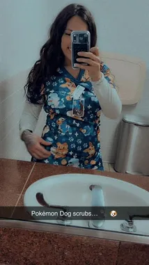 In a candid moment captured in her bathroom, Sasha takes a mirror selfie. She is dressed in a distinctive blue top adorned with cartoon characters and paw prints, layered over a white long-sleeved shirt. With long dark hair framing her face, she holds her phone up to frame the shot, creating a personal and relatable snapshot of her day. by @squashha with original sound