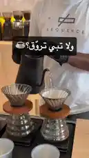 This video provides a close-up, step-by-step demonstration of the pour-over coffee brewing method. A barista, wearing black gloves and a white t-shirt with the 'SEQUENCE' logo, carefully pours hot water from a gooseneck kettle over ground coffee in a V60 dripper. The process is shown on a digital scale, emphasizing precision. This visual guide is ideal for anyone looking to learn the art of manual coffee brewing. by @sequence-coffee with Hinoki Wood by Gia Margaret
