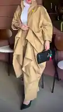 This video showcases a full-length fashion look from Artal Fashion أرتال. A model presents a stylish ensemble featuring a long, structured khaki trench coat with dramatic ruffled layers over matching wide-leg trousers. The outfit is paired with a white turtleneck, black pointed-toe heels, and a textured black clutch adorned with a colorful charm. The setting is a modern indoor space with wooden chairs, highlighting the contemporary design and elegant silhouette of the clothing. by @artal.street with original sound