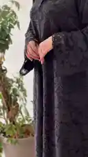 A woman elegantly models a full-length black lace abaya, showcasing its intricate details. She accessorizes with a vibrant green velvet clutch and a stylish white shopping bag from 'Khial Abaya'. The video highlights the outfit from multiple angles, emphasizing the texture of the fabric and the overall sophisticated look. by @mohammed_aldrop with Original Sound by mohammed_aldrop