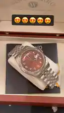A close-up showcase of a new West End watch in its branded box. The timepiece features a distinctive reddish-brown dial with Arabic numerals, day, and date complications, all presented on a silver Jubilee-style bracelet. A voiceover in Arabic describes the watch as a beautiful new model from the brand. by @lussowatches with Original Sound by lussowatches