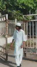 A man dressed in a traditional white kurta and matching cap walks through an old, rusted metal gate in a sunlit outdoor setting. He adjusts his hair and cap as he moves forward, showcasing a calm demeanor. The scene captures the essence of everyday life with a focus on cultural attire and rustic surroundings. by @lil.ishhhh with Original Sound by Contains: Afghan Jalebi (Film Version) - Akhtar Channal