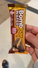 A close-up look at a Bombbar Wafers protein bar, highlighting its packaging details such as '22% Protein' and 'Hazelnut Ice Cream' flavor. The creator discusses the importance of balance and moderation in diet, suggesting this sweet treat as a guilt-free indulgence. by @bbbbb with Original Sound by bbbbb