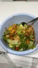 A close-up view of a light blue bowl filled with a colorful salad containing lettuce, diced vegetables, and other ingredients. A spoon is used to mix the salad, and creamy dressing is added from a bottle. The person preparing the salad speaks in Arabic, expressing excitement about the deliciousness of the meal. This simple yet appetizing recipe demonstrates a quick way to prepare a healthy and tasty salad. by @alafasy81 with Original Sound by alafasy81