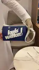 A close-up showcase of a blue Louis Vuitton pouch bag with white branding and strap. A person in a white outfit displays the bag from multiple angles, highlighting its design and size. An Arabic voiceover describes the product as 'nice' and states its price is 7,500. by @lussowatches with Original Sound by lussowatches