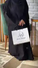 This stylish video features a model showcasing a beautiful black abaya from the brand 'Khial Abaya'. The piece is highlighted with elegant leaf-shaped embellishments and is paired with modern sandals. The model gracefully poses and turns, allowing viewers to appreciate the garment's design and flow. The setting includes a green chair and a brick wall, creating a chic and contemporary atmosphere. by @mohammed_aldrop with Original Sound by mohammed_aldrop