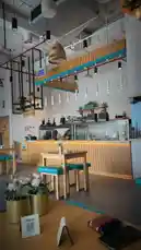A stylish tour of a contemporary cafe interior, showcasing wooden tables, blue cushioned stools, and unique hanging light fixtures. The space features a clean white brick wall backdrop and a well-lit counter area, creating a welcoming and trendy atmosphere perfect for modern coffee shops. by @dsunmusic with Original Sound by dsunmusic