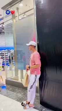 Watch Aman Malik in a relaxed shopping moment, showcasing a stylish and comfortable outfit. He's wearing a pink t-shirt, white Adidas track pants with black stripes, a white baseball cap, and slide sandals. Holding a paper shopping bag, he stands near a store entrance in a modern mall setting. This look is perfect for casual outings and everyday style inspiration. by @officialaman08 with Original Sound by Contains: Stand By - Deep Chahal, Bugzy
