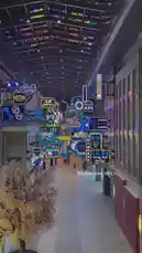 Experience the electric atmosphere of a modern shopping mall in Dubai after dark. This high-angle view captures a dazzling array of colorful neon signs, including prominent 'Wong Sai Bridal' and 'Kung Fu Panda' branding, illuminating a bustling pedestrian walkway. The scene, set against a backdrop of contemporary architecture and autumnal trees, offers a glimpse into the city's dynamic nightlife and retail culture. by @dsunmusic with Original Sound by dsunmusic