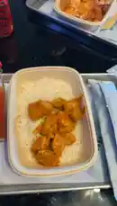 In this casual food vlog, a man enjoys a delicious meal of chicken tikka masala served over rice. He mixes the dish with a spicy red sauce, creating a vibrant and appetizing plate. The setting appears to be a modern restaurant or cafe with large windows, adding to the relaxed dining atmosphere. by @bbbbb with Original Sound by bbbbb