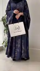 A woman models a stunning blue abaya with a unique tie-dye pattern, accessorized with a black hijab and elegant shoes. She holds a white shopping bag from 'Khial Abaya,' showcasing the brand's latest design. The video highlights the flowing fabric and stylish details of the garment. by @mohammed_aldrop with Original Sound by Contains: Garee2a Awy - A COLORS SHOW - TUL8TE, COLORS