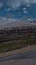 This captivating video captures a scenic drive along a winding mountain road. From the perspective of a moving vehicle, viewers see vast, snow-covered peaks under a dramatic sky, lush green valleys, and roadside structures like a small orange-roofed building and a red tent. The journey unfolds through a breathtaking alpine landscape, showcasing the raw beauty of nature. by @moazzam with Main to hun yahan💞🥀 by Contains: Faasle - Kaavish & Quratulain Balouch