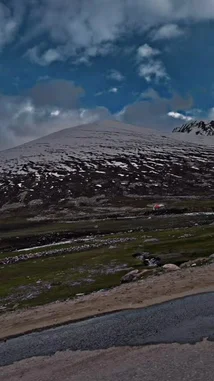 This captivating video captures a scenic drive along a winding mountain road. From the perspective of a moving vehicle, viewers see vast, snow-covered peaks under a dramatic sky, lush green valleys, and roadside structures like a small orange-roofed building and a red tent. The journey unfolds through a breathtaking alpine landscape, showcasing the raw beauty of nature. by @moazzam with Main to hun yahan💞🥀 by Contains: Faasle - Kaavish & Quratulain Balouch