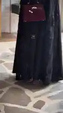This stylish fashion video features a model showcasing a beautiful black abaya with intricate floral embroidery and sequins. She pairs it with a chic burgundy handbag and elegant sandals, presenting various poses and angles against a modern white brick wall background. The look is completed with a matching hijab, highlighting contemporary modest fashion. by @mohammed_aldrop with Original Sound by mohammed_aldrop