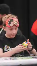 A young boy attempts a blindfolded Rubik's cube solve during a competition, followed by a man in a home setting trying to solve a puzzle using tape. The video captures two distinct challenges involving problem-solving under unique constraints. by @elqaq with Original Sound by elqaq