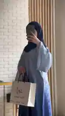 A woman models a stunning blue gradient abaya from Khilal Abaya, showcasing its elegant design and flow. She holds a branded shopping bag, highlighting her purchase. The video captures her from multiple angles against a white brick wall, emphasizing the garment's details and luxurious fabric. by @mohammed_aldrop with Original Sound by mohammed_aldrop