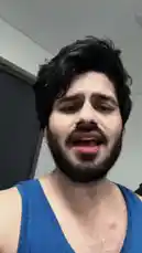 A man with dark, curly hair and a beard, wearing a blue tank top, sings passionately while performing exercises in a home gym setting. He smiles and shows effort, creating an energetic and motivational atmosphere. by @dsunmusic with Original Sound by dsunmusic