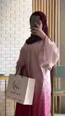 A stylish woman models a beautiful pink ombre abaya, transitioning from light pink to deep red, paired with a matching hijab. She carries a branded 'Khial Abaya' shopping bag, highlighting the brand's elegant design and quality fabric. The video focuses on showcasing the flowing silhouette, intricate details, and graceful movement of the traditional attire. by @mohammed_aldrop with Original Sound by Contains: Hashak Men Al Sedq - حشاك من الصدك - Bassnan Al Khateeb | Khaled Al Hanin - بسمان الخطيب | خالد الحنين 