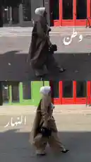 A woman wearing a hijab walks confidently down a city street, showcasing elegant modest fashion from Artal Fashion's new collection. The split-screen visual highlights a stylish brown coat and wide-leg pants ensemble, emphasizing contemporary design and cultural expression. Text overlays announce 'New Collection Coming Soon' and feature Arabic script ('وَطن', 'النِّمار'), suggesting a theme of heritage and modernity. This look embodies the fusion of traditional values with current street style trends. by @artal.street with original sound