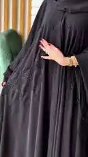 A woman models a sophisticated black abaya with intricate beadwork, showcasing its elegant design while holding a refreshing drink and a branded shopping bag. The stylish outfit is presented in a modern indoor setting, highlighting a chic and contemporary fashion look. by @mohammed_aldrop with Original Sound by mohammed_aldrop