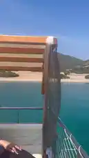 Experience a serene journey along a stunning coastline, viewed from the deck of a boat. The crystal-clear turquoise water gently laps against the hull as you sail past lush green hills and a sandy beach under a bright blue sky. This tranquil scene captures the essence of a perfect day out on the open sea. by @codedsoso with Original Sound by codedsoso