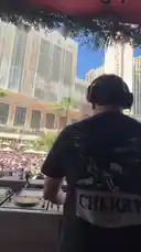 The renowned DJ Tiesto commands the stage at a massive outdoor pool party in Las Vegas. Wearing headphones and a black t-shirt, he performs for a huge, energetic crowd gathered in front of the Bellagio hotel. The sun is shining brightly, and the iconic Las Vegas skyline serves as a stunning backdrop. by @tiesto with Original Sound by tiesto