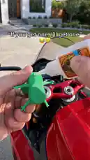 This fun and quirky video shows a person attaching a green spring frog toy to the handlebars of a red motorcycle. The text overlay 'If you get one, I'll get one' suggests a playful challenge. The video then cuts to various shots of the spring frog bouncing on different motorcycles while being ridden, demonstrating its durability and entertainment value. by @uk-gos with Original Sound by Contains: Free Bird - MOONLGHT