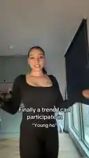 A woman in a black outfit dances energetically in her apartment to a trending audio clip. She smiles at the camera while performing the 'Young ho' dance challenge, with on-screen text confirming she is participating in the trend. by @n8ka_122 with Original Sound by n8ka_122